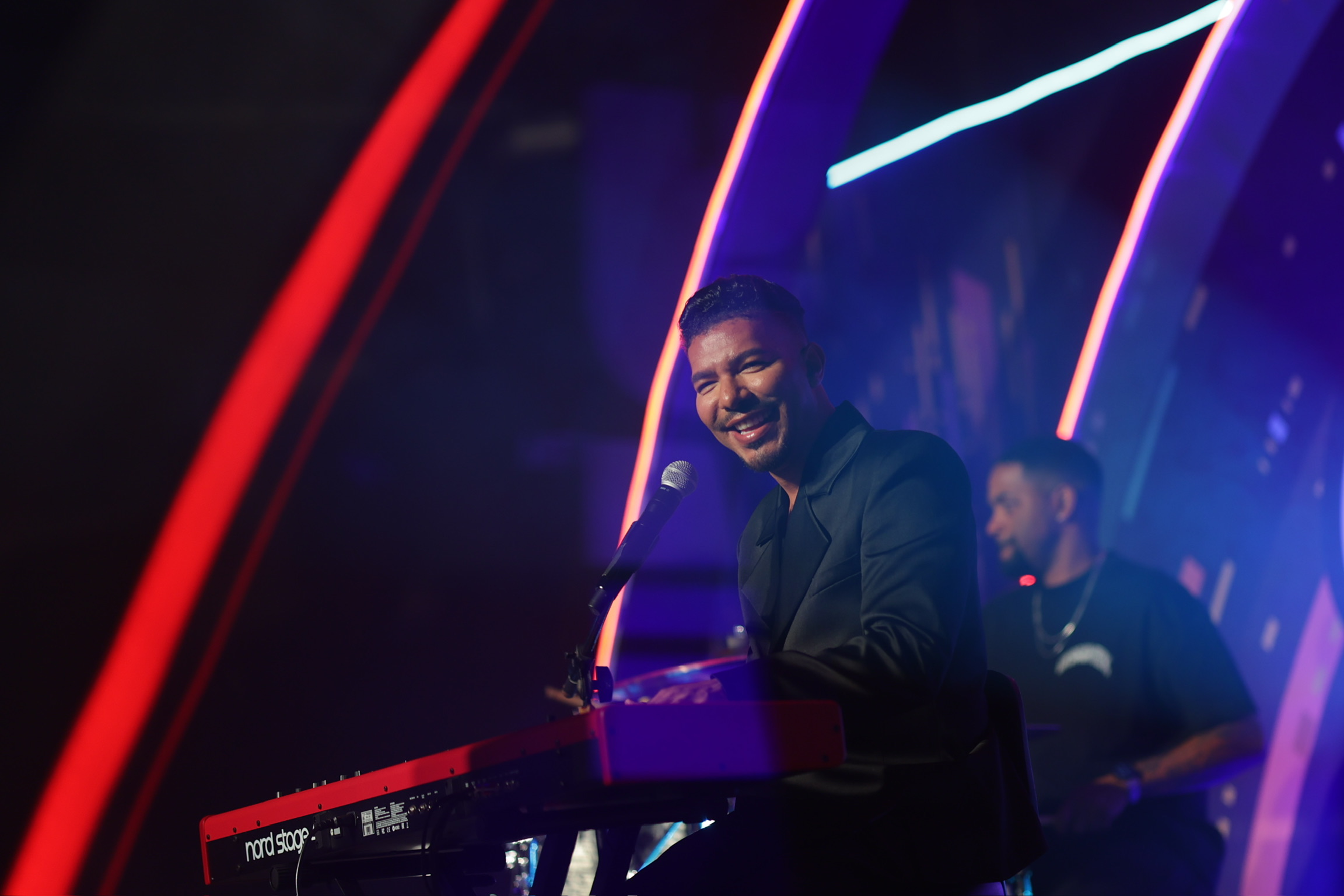 Stevie Mackey smiling at the keys on stage, with the band behind him